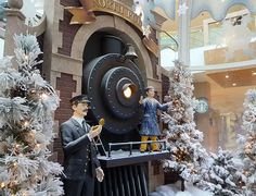 two men are standing next to a fake train in a building with snow on the ground