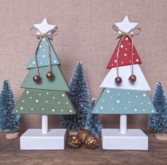 three wooden christmas trees with bells and ornaments on top of each tree, one decorated in different colors