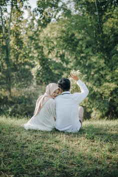 a man and woman sitting on top of a grass covered field next to each other