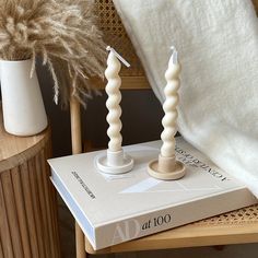 two candles sitting on top of a book next to a vase with dried grass in it