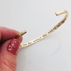 a hand holding a gold cuff with writing on it and a red manicured nail