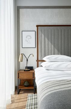 a bed sitting next to a window with white curtains and pillows on top of it