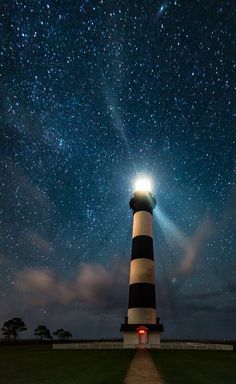 a lighthouse under the night sky with stars in the background and light shining on it