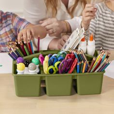 two women sitting at a table with pencils, markers and pens in a container