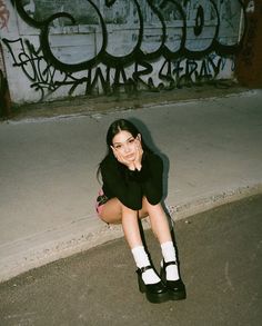 a woman sitting on the ground in front of graffiti