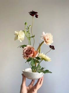 a person holding a white bowl with flowers in it and the bottom half of their hand