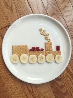 a white plate topped with crackers and bananas on top of a wooden table next to an image of a train