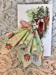 a greeting card with an image of a woman in a green dress on a lace tablecloth