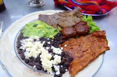 a white plate topped with meat, beans and guacamole on top of a table