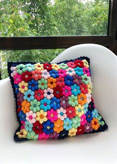 a crocheted pillow sitting on top of a white chair next to a window