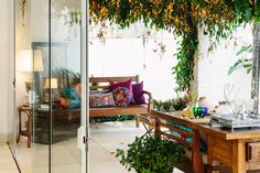 a room with a table, couch and potted plants on the outside wall next to glass doors