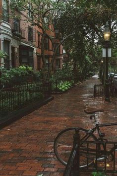 a bicycle parked on the side of a brick road next to a lamp post and fence