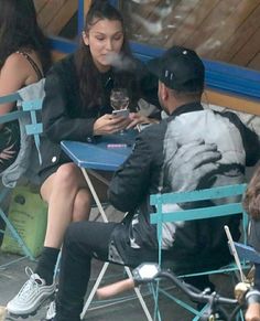 a man and woman sitting on blue chairs looking at their cell phones in front of them