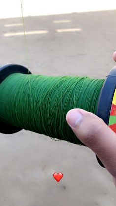 a hand holding a spool of green thread with a red heart on the end