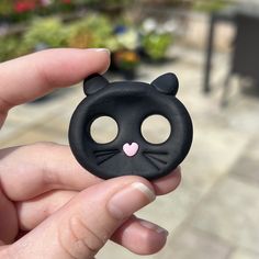 a hand holding a black cat toy with a pink heart on it's nose