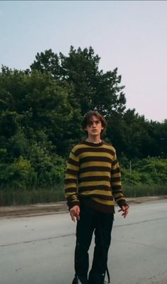 a young man riding a skateboard down a street next to tall grass and trees