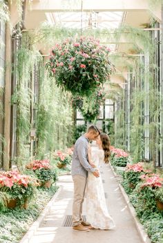 an engaged couple standing in the middle of a greenhouse surrounded by flowers and greenery