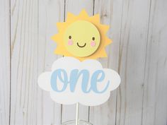 a cake topper with the word one on it and a smiling sun above it