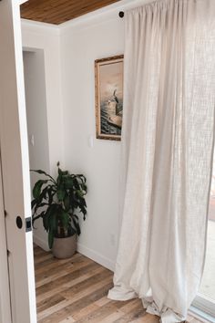 a white curtain is hanging in front of a window with a potted plant next to it