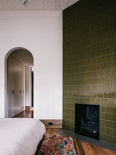 a room with a bed, fireplace and green tiles on the wall above it is a rug