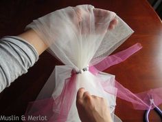 someone is wrapping something up on a table with some pink organe and white fabric