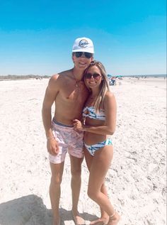 a man and woman in bathing suits on the beach posing for a photo with their arms around each other