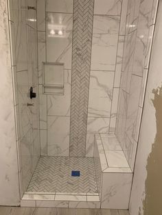 a walk in shower sitting next to a toilet and wooden floored bathroom wall with white marble tiles on the walls