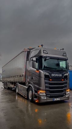 a semi truck parked in a parking lot on a rainy day with dark clouds overhead