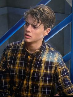 the young man is wearing a plaid shirt and looking at something in his hand as he talks to someone