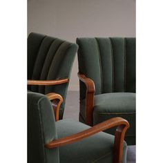 two green upholstered chairs sitting next to each other in front of a white wall