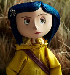 a doll with blue hair wearing a yellow hoodie in the middle of tall grass