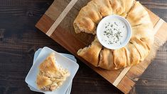 a wooden cutting board topped with pastry next to a bowl of dip