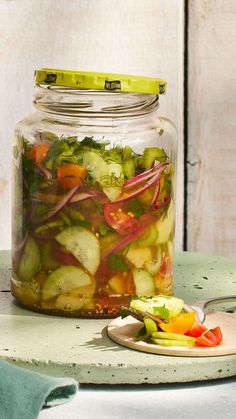 a glass jar filled with vegetables sitting on top of a table next to a cutting board