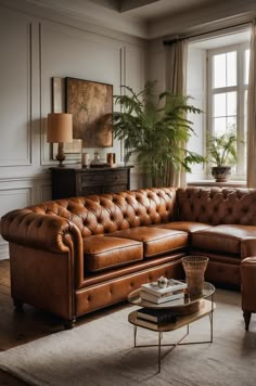 a brown leather couch sitting in front of a window next to a chair and table