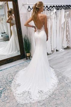 a woman standing in front of a mirror wearing a white wedding dress with open back