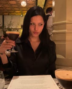 a woman sitting at a table with a glass of wine in her hand and menu on the table