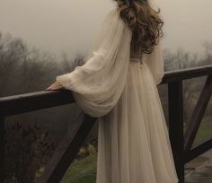 a woman is standing on a bridge with her back to the camera, wearing a long white dress