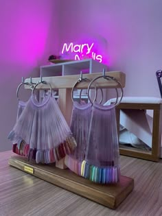 three pairs of colorful skirts hanging from hooks on a wooden stand in front of a purple neon sign