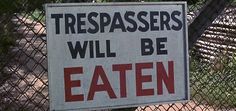 a sign that says trespassers will be eaten behind a chain link fence with trees in the background