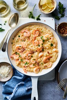 pasta with shrimp and parmesan cheese in a skillet next to wine glasses