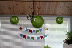 three green paper lanterns hanging from the ceiling above a table with plants and decorations on it