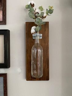 there is a bottle with flowers in it hanging on the wall next to two framed pictures