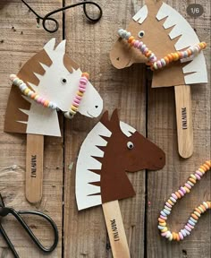 three horse puppets made out of popsicle sticks on top of a wooden table next to scissors