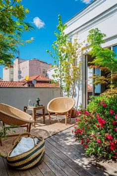 two wicker chairs sitting on top of a wooden deck next to flowers and trees