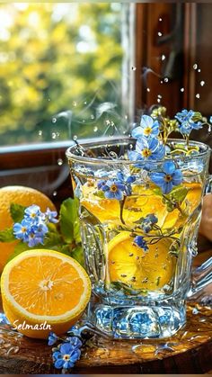 a glass cup filled with water next to sliced oranges and blue forgeter flowers