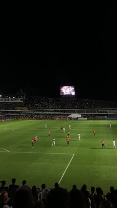 a group of people playing soccer on a field at night with lights in the background