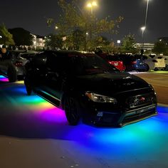 a black car is parked in the parking lot with colorful lights on it's side