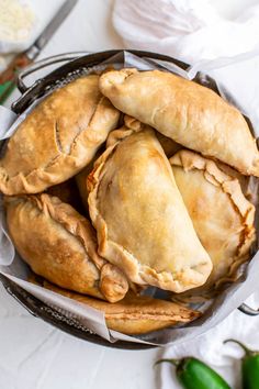 several baked pastries in a basket on top of a white tablecloth with green leaves