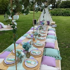 a long table set up with place settings for dinner in the grass, surrounded by flowers and greenery