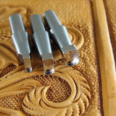 three metal handles sitting on top of a brown leather surface with intricate designs and curves